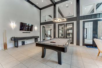 A billiard table is in the middle of a room with a TV and a bench.